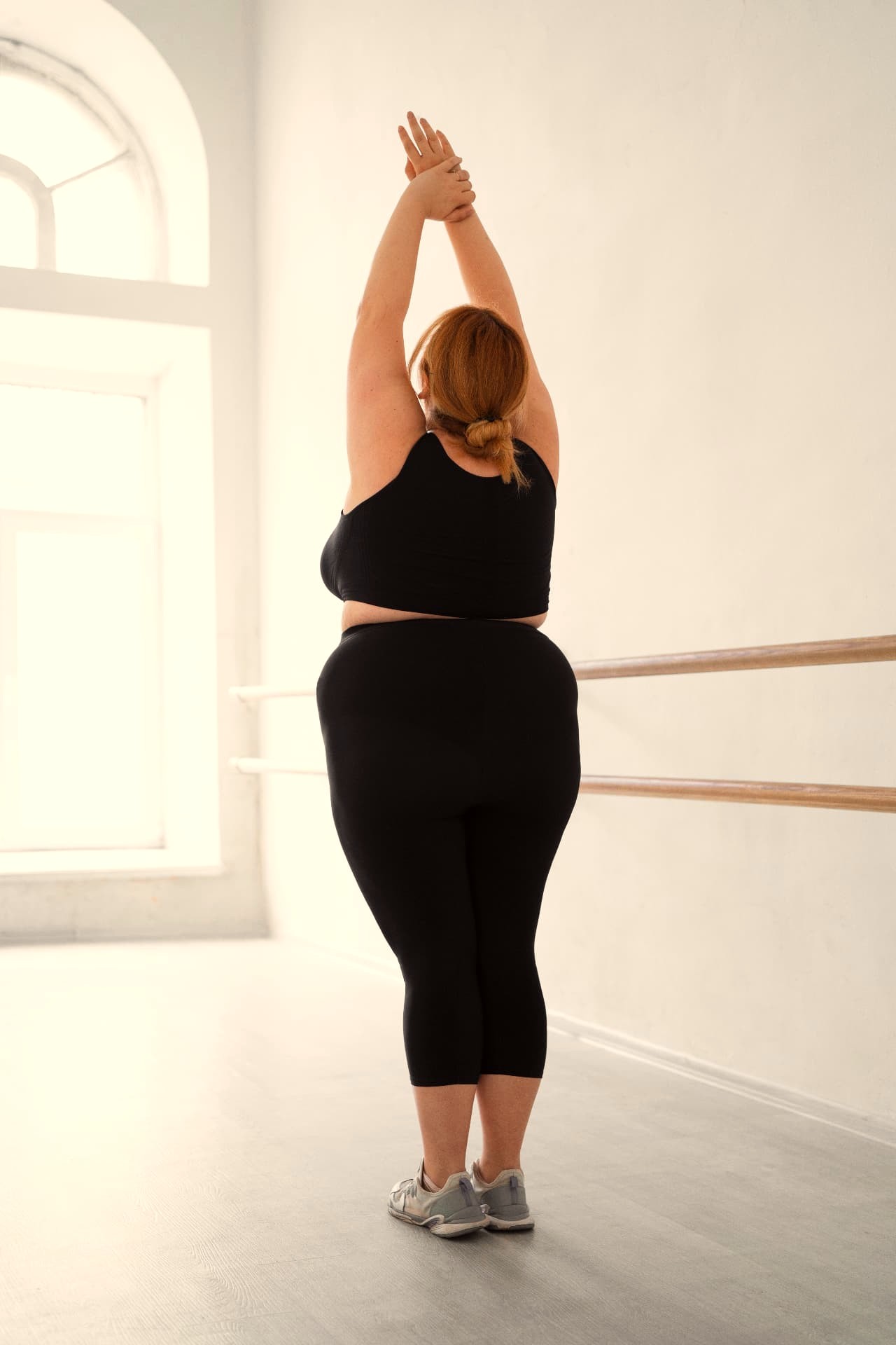 A dancer stretching tall in a bright studio in black compression leggings